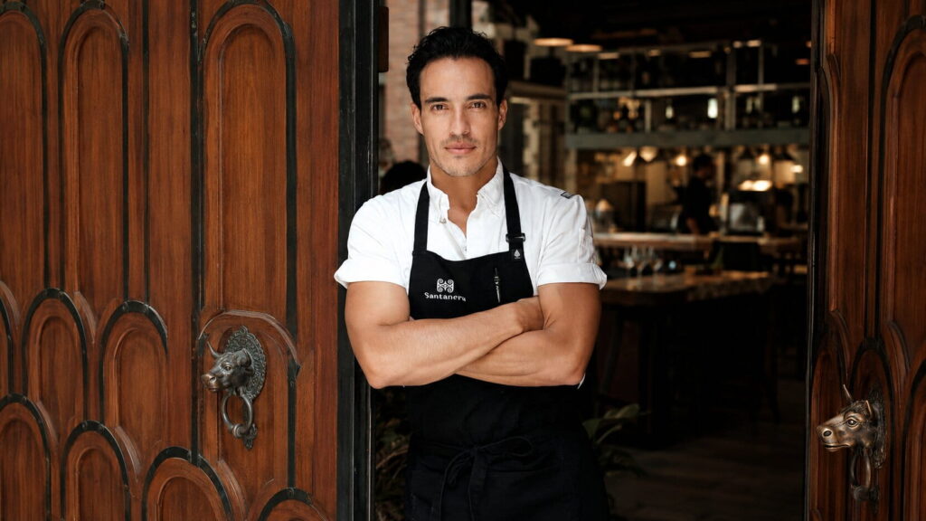 Chef Andr&eacute;s Becerra standing in a restaurant wearing a black apron