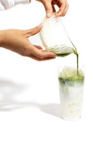 Matcha being poured into a glass of milk as part of a wellness ritual