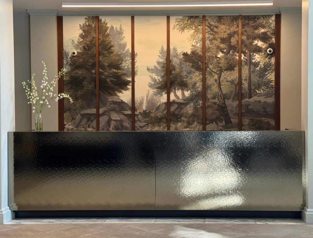 Hotel reception desk with a forest mural and dark textured counter