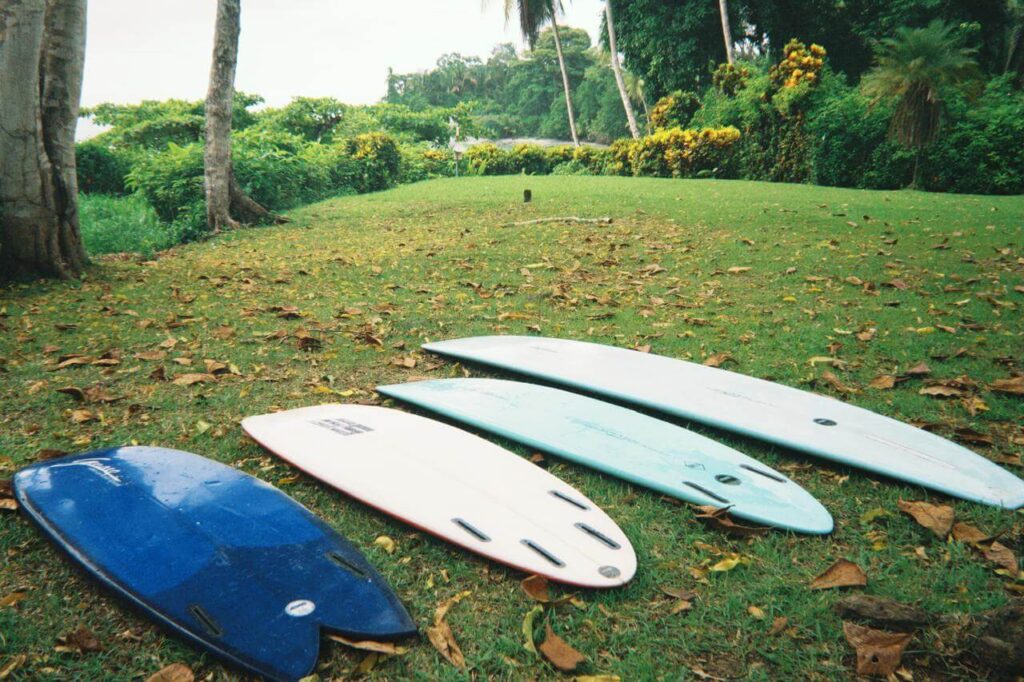 A collection of surfboards laid out on the sand at Bodhi Surf + Yoga, including large soft-top foam boards for beginners and sleek fiberglass funboards for intermediate surfers.