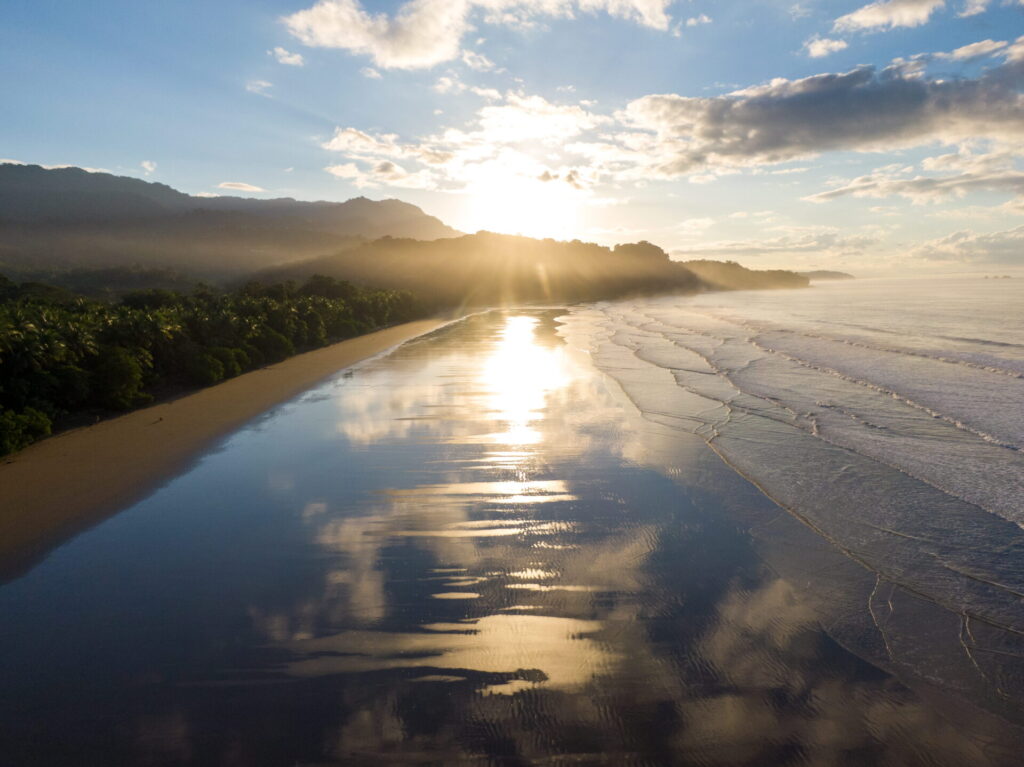 A calm, glassy morning ocean at Playa Uvita during the green season, with smooth waves peeling perfectly under a clear sky.