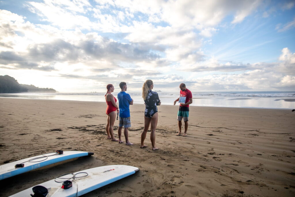 An instructor and student standing on the beach at Playa Uvita pointing toward the waves, reading the wind direction and tide before entering the water.