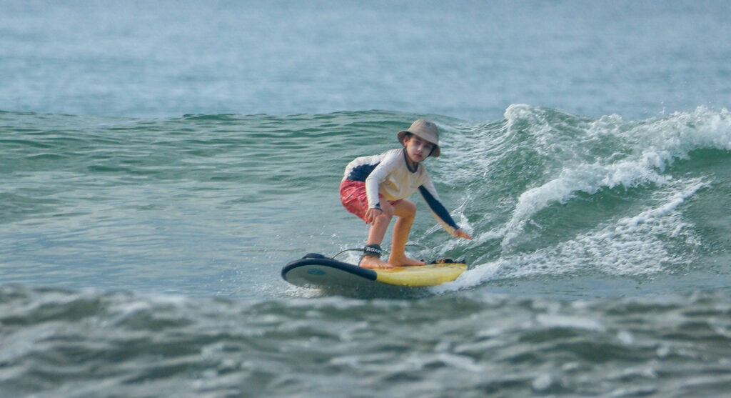 Child surfing blue/green waves in Uvita, Osa, Costa Rica