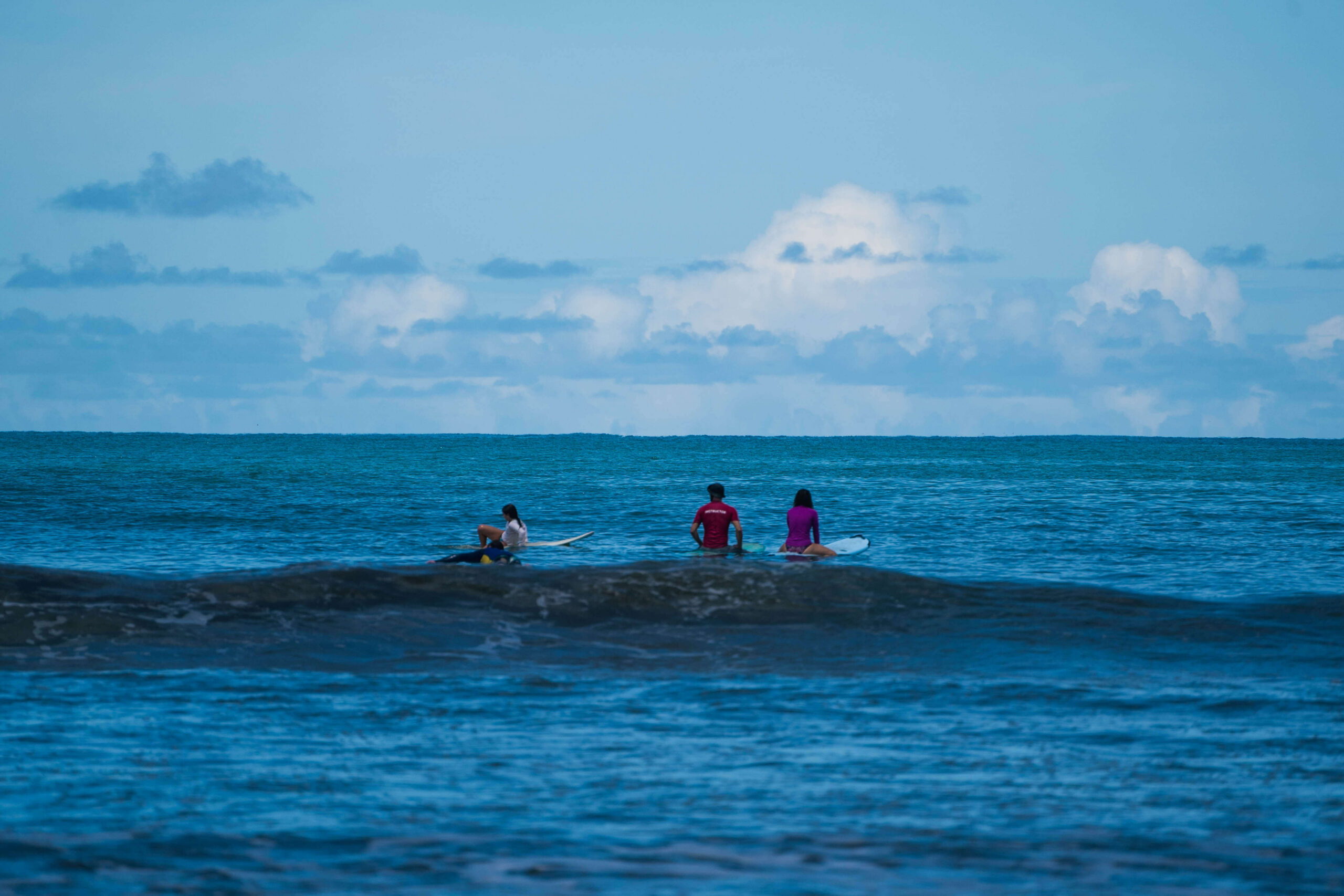 A group of surfers sitting on their boards in the ocean lineup, smiling and sharing a moment of community and Pura Vida.