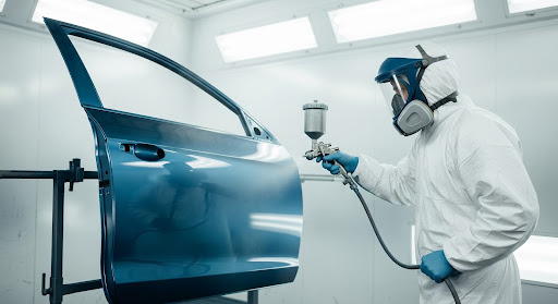 A professional technician auto painting a car in a safe, clean paint booth.