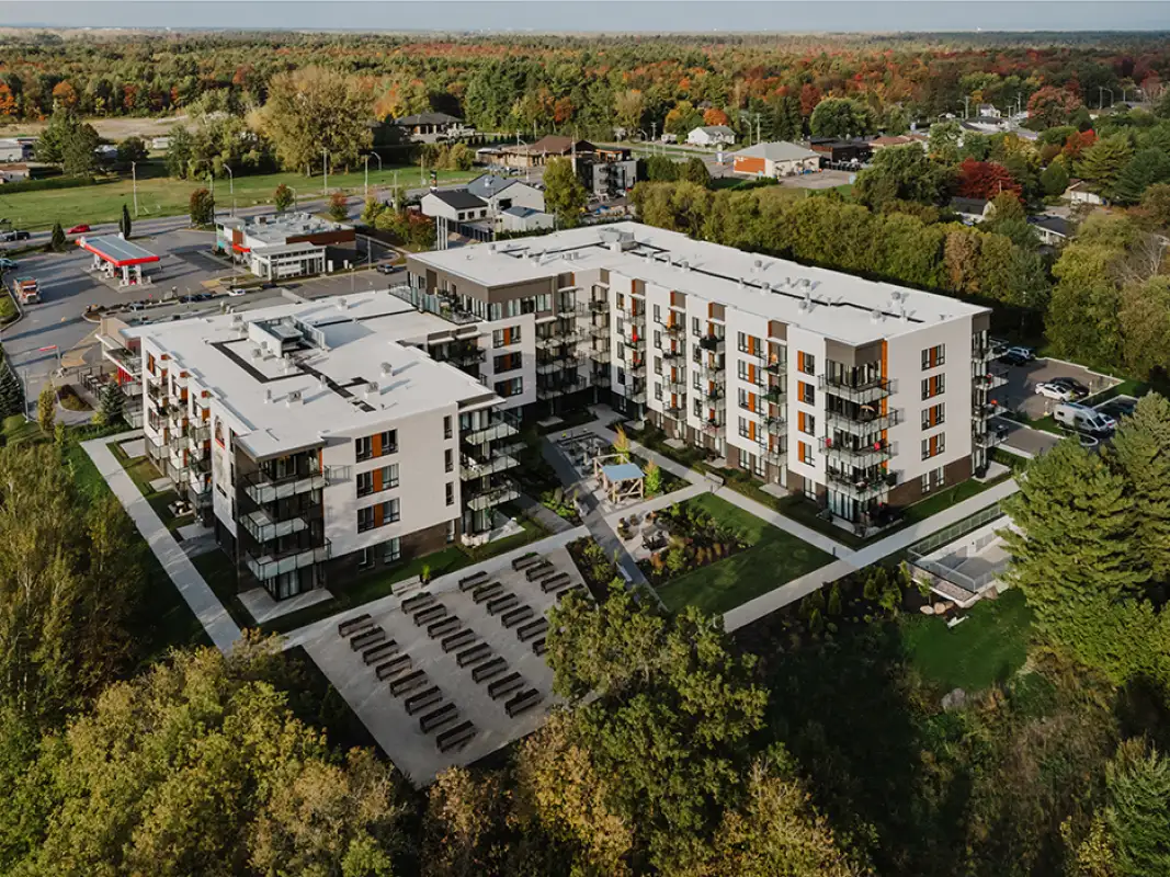 Vue aérienne d’un immeuble d’appartements contemporains avec balcons, jardins aménagés et espace extérieur, situé dans un quartier verdoyant