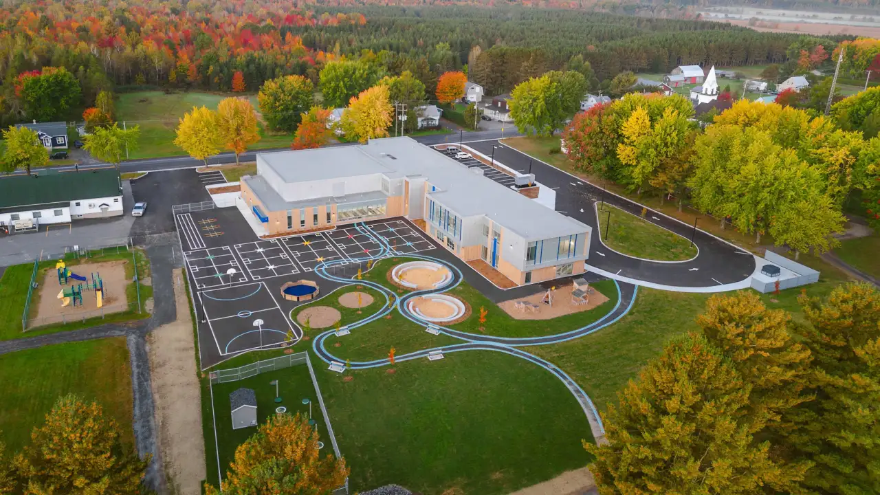 Vue aérienne de l’École des Deux-Rivières avec cour d’école moderne, aires de jeux éducatives et environnement naturel aux couleurs automnales au Québec.
