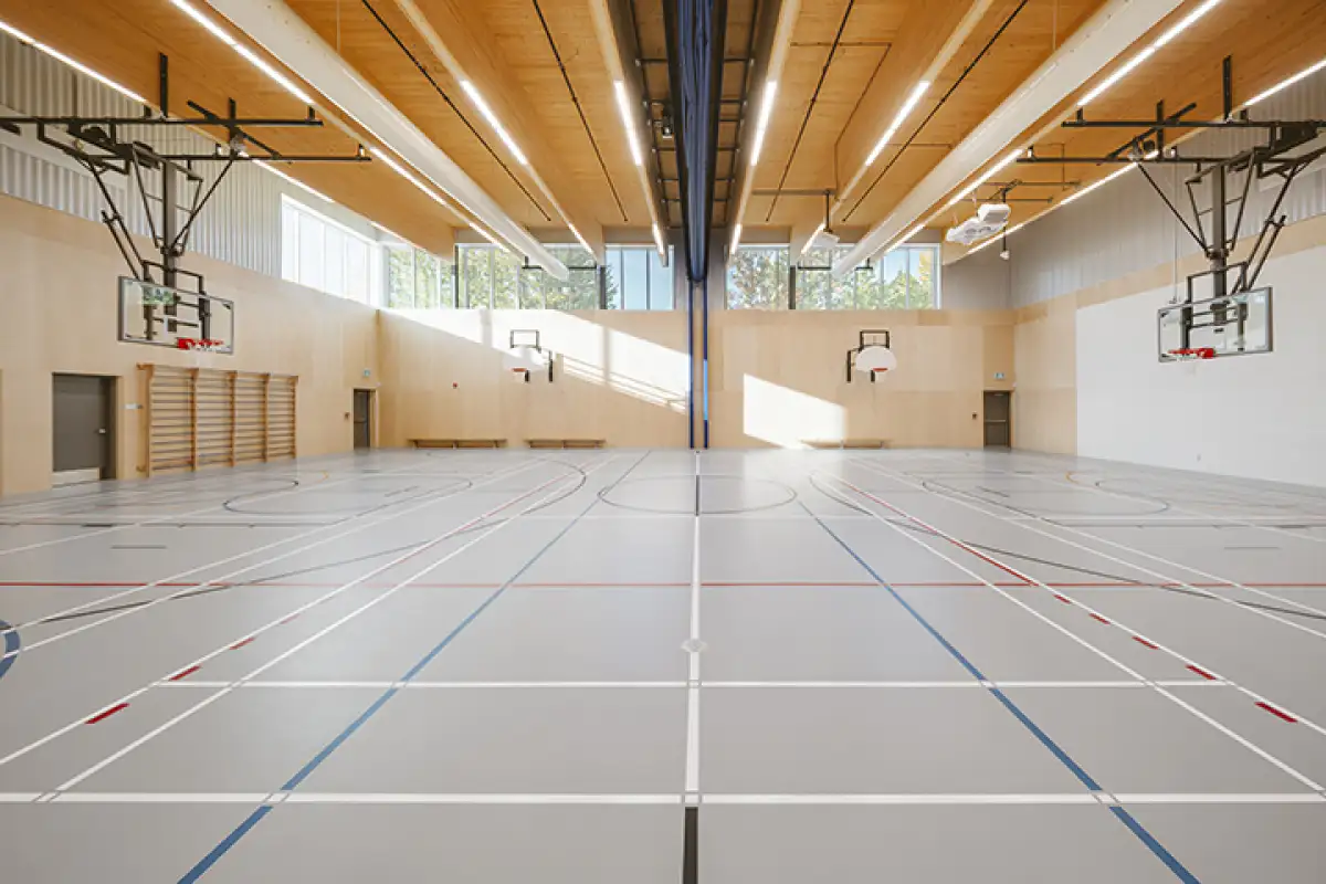 Grand gymnase multifonction de l’École des Deux-Rivières avec terrain sportif intérieur, plafond en bois et éclairage naturel abondant.