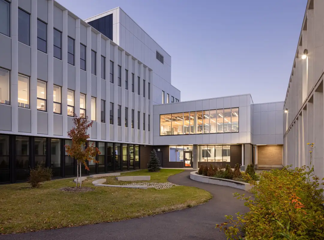 Cour intérieure de l’École Cardinal-Roy avec passerelle vitrée, aménagement paysager et architecture scolaire contemporaine favorisant la lumière naturelle.