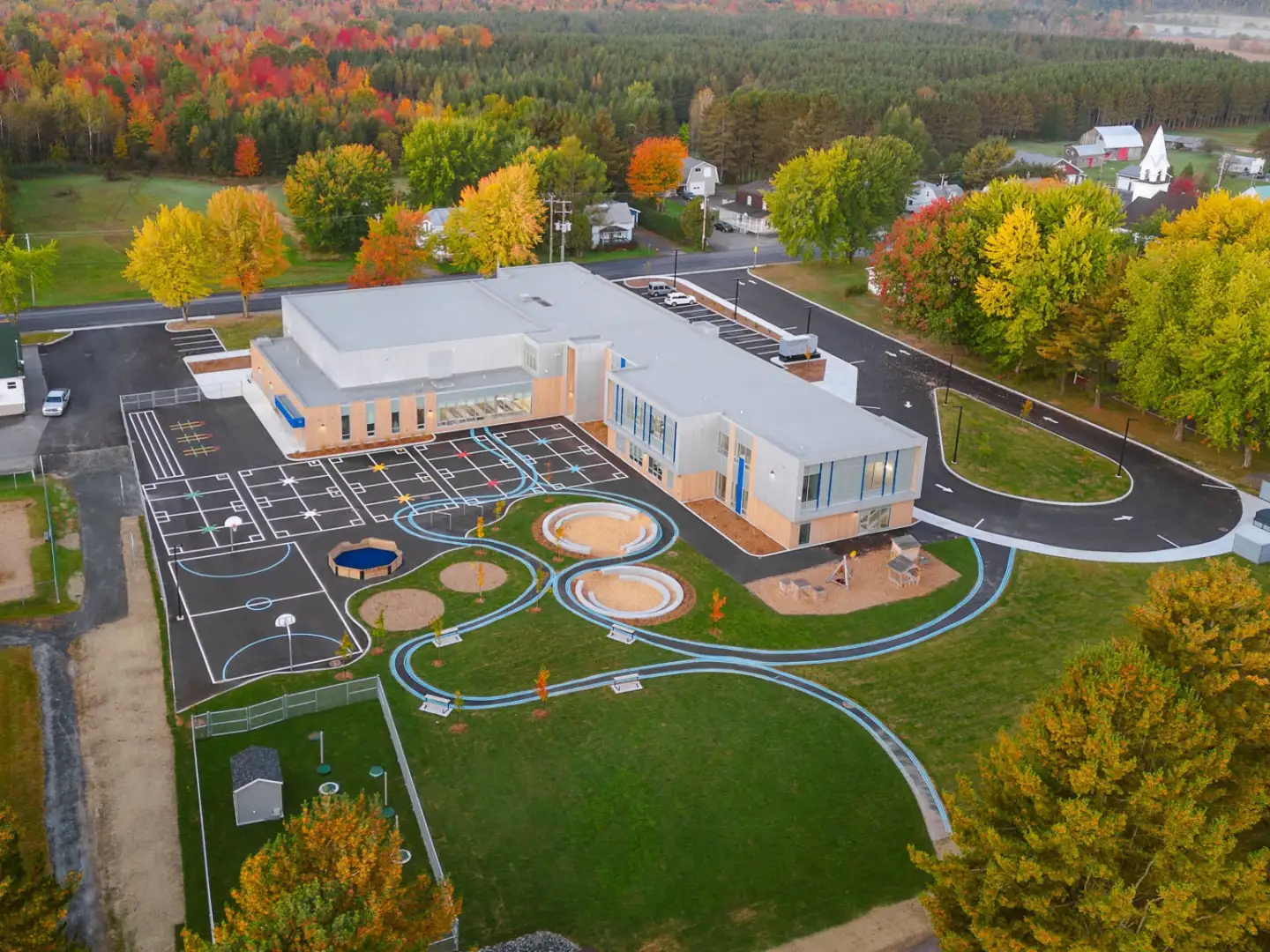 Vue aérienne de l’École des Deux-Rivières avec cour d’école moderne, aires de jeux éducatives et environnement naturel aux couleurs automnales au Québec.