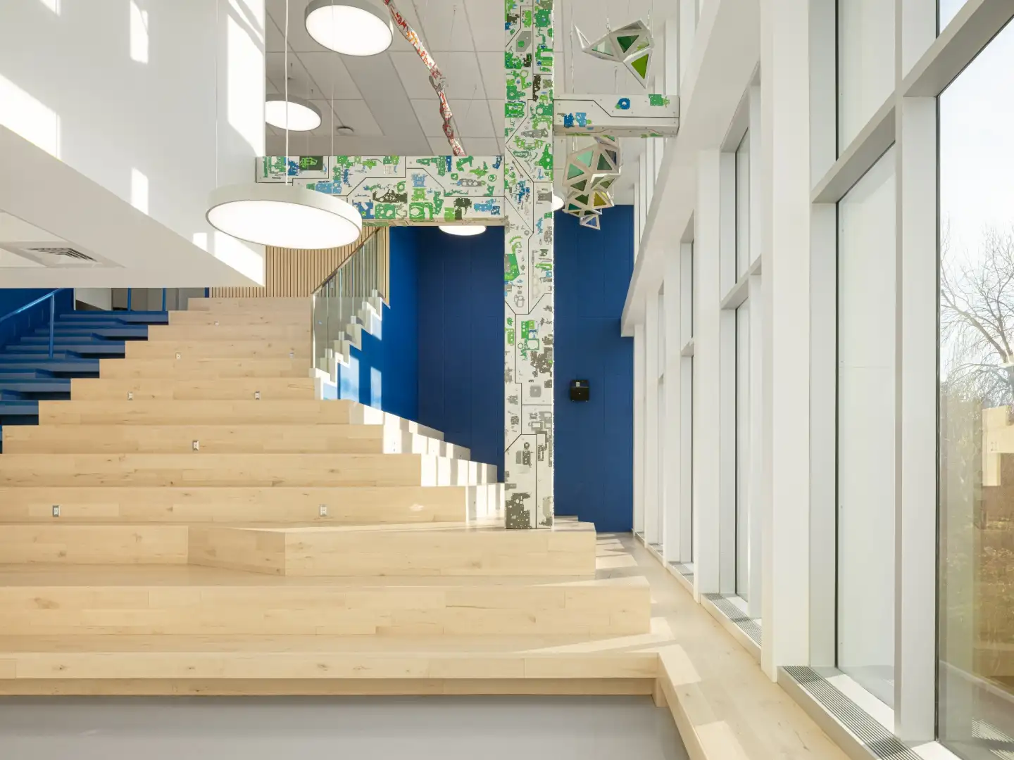 Agora lumineuse de l’École Cardinal-Roy avec gradins en bois, grands vitrages et espaces collaboratifs favorisant les échanges et l’apprentissage.