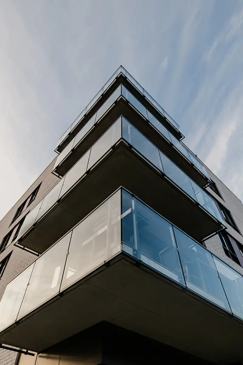 Détail architectural d’un bâtiment contemporain à plusieurs étages avec grands balcons en verre, photographié en contre-plongée