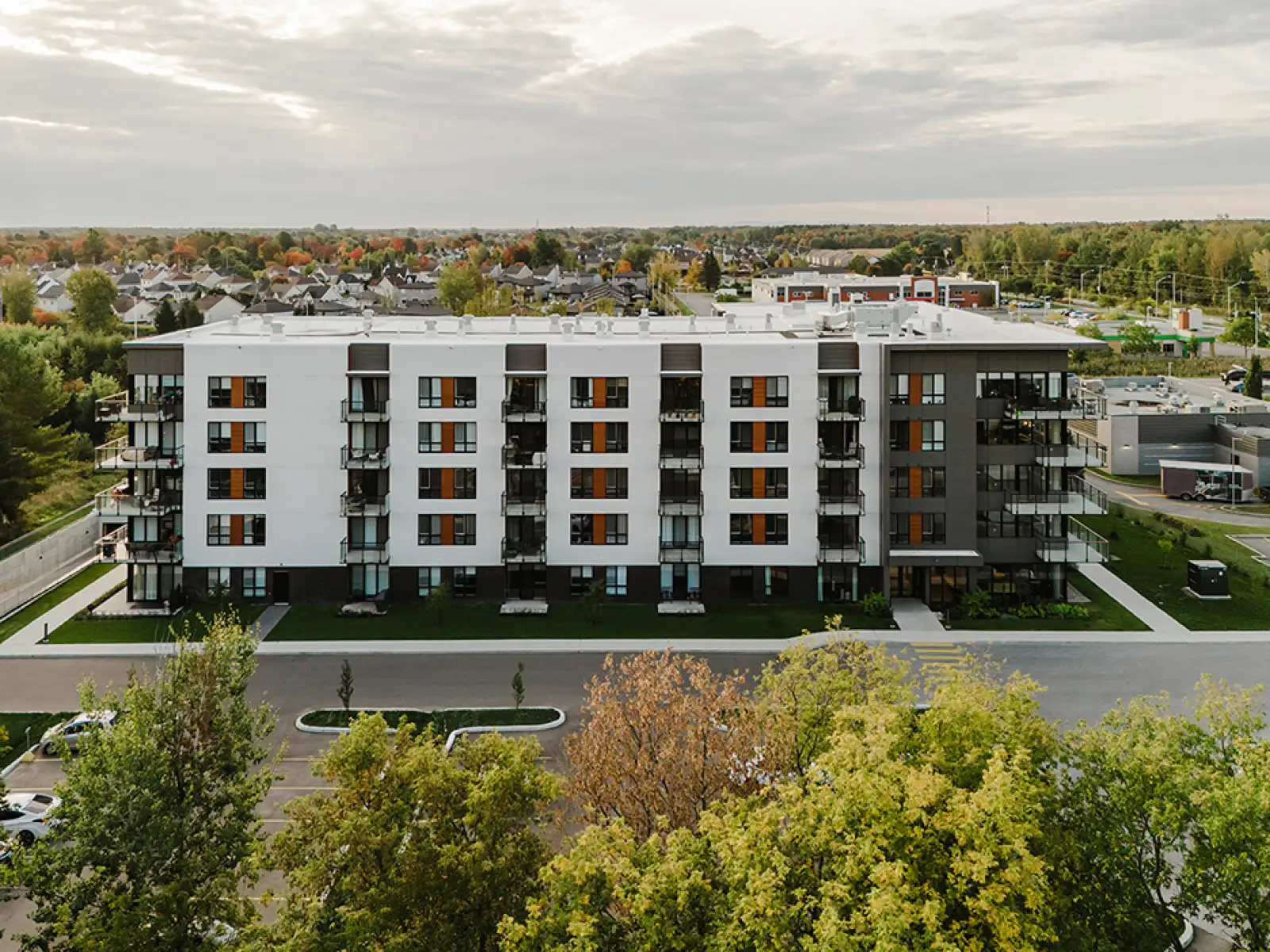 Immeuble d’appartements contemporains à cinq étages, avec façades blanches et balcons en verre, entouré d’arbres dans un quartier résidentiel