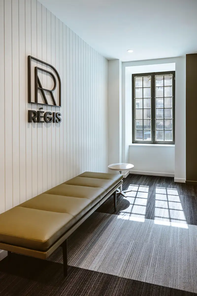 Corridor lumineux avec un banc de repos en cuir olive, ajoutant une touche chaleureuse et élégante à l’espace au design épuré.