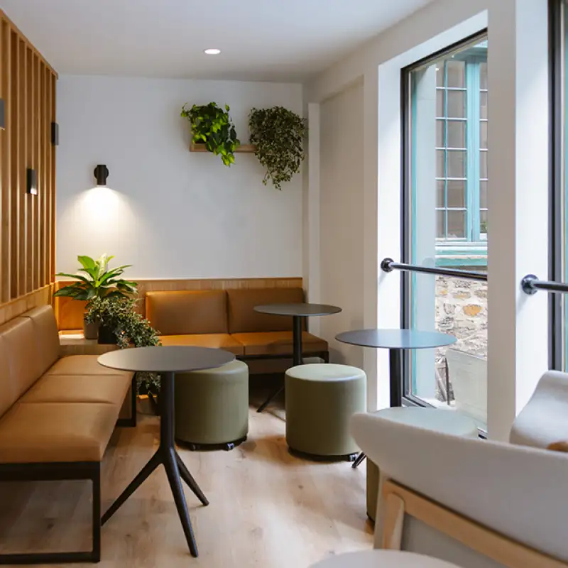 Salle de détente lumineuse avec une grande fenêtre, une table moderne et un tabouret, offrant un espace convivial et épuré.