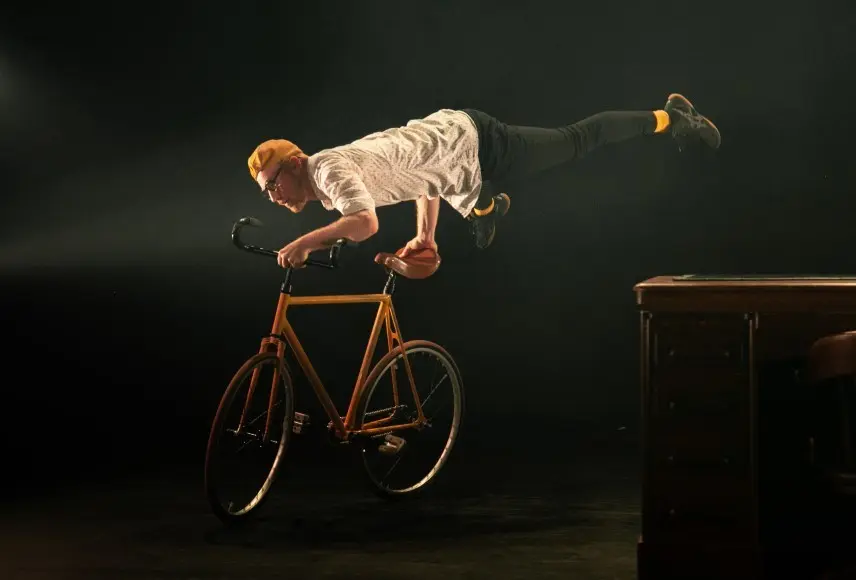 L'acrobate Guillaume Doin se tient en équilibre sur un vélo, les mains sur le guidon et la selle, les jambes dans les airs.