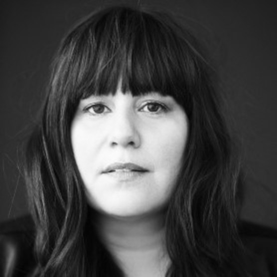 Photo en noir en blanc de Sarah. Elle regarde l'objectif, elle a les cheveux longs, foncés avec un toupet.