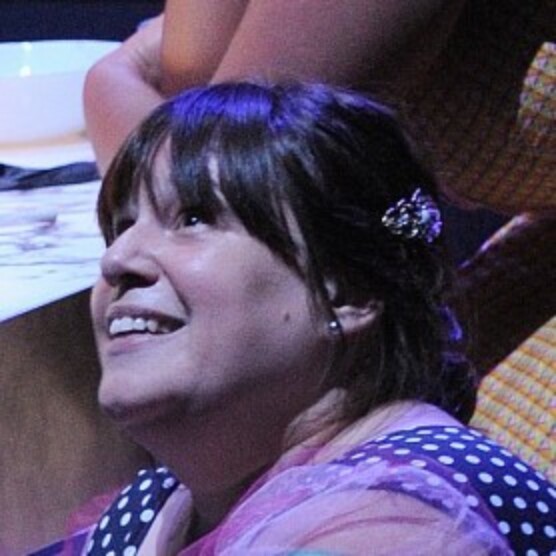 Amelia sourit en regardant vers le haut en souriant. Elle a les cheveux attachés et porte un habit rose et à pois.