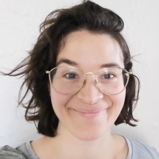 Photo sur fond blanc d'Agathe, une femme au teint clair, aux yeux bruns et aux cheveux bruns droits coiffés vers la gauche. Elle porte un haut gris, des lunettes rondes à monture fine et sourit en regardant la caméra.