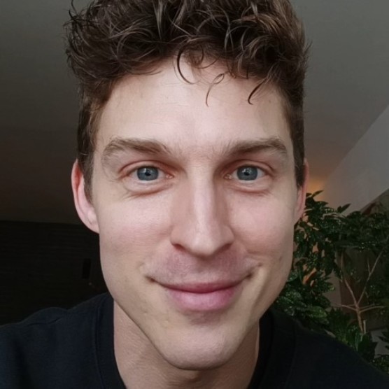 Photo de Xavier, un homme au teint clair, aux yeux bleus et aux cheveux châtains courts ondulés. Il porte un haut noir et regarde la caméra en souriant.