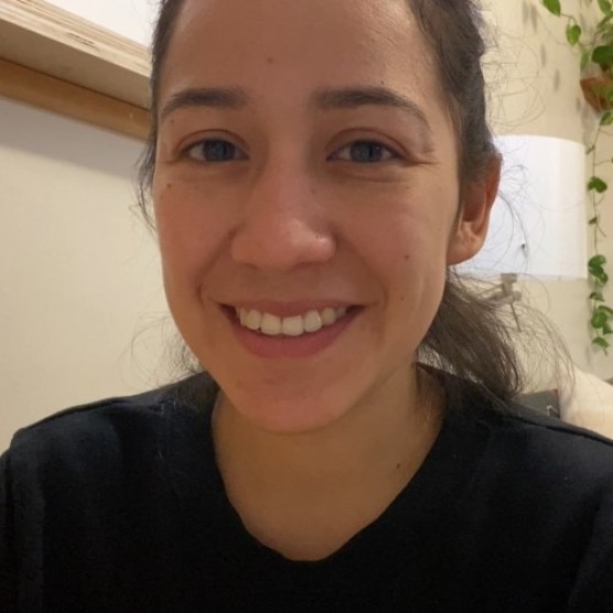 Photo de Yuma, une femme au teint moyen-clair, aux yeux bruns et aux cheveux foncés attachés. Elle porte un chandail noir et regarde la caméra en souriant.