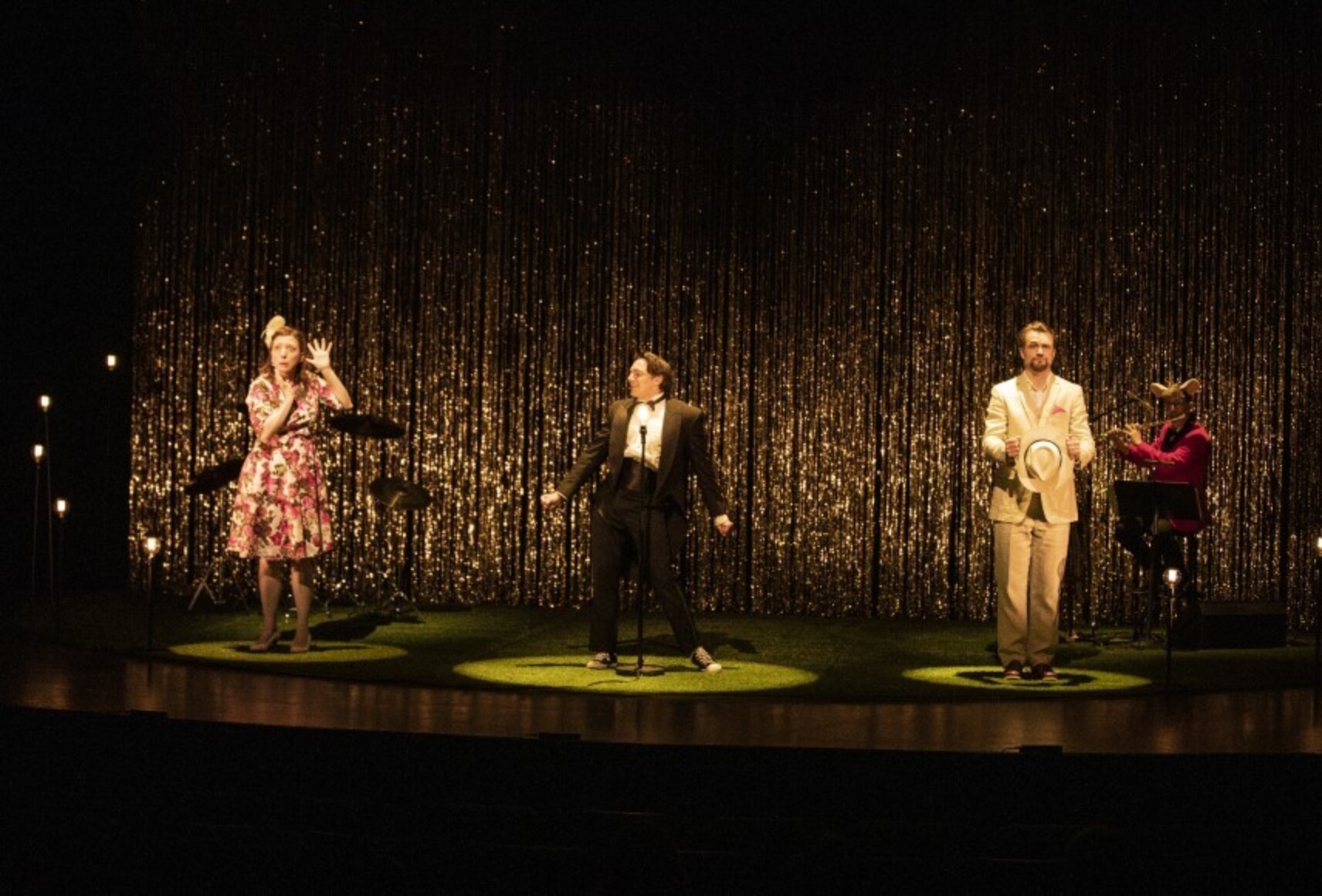 Trois artistes, à gauche une femme avec une robe fleurie, au centre un homme en tuxedo noir et blanc, à droite un homme avec un complet beige dans des poses expressives. Derrière eux, un musicien joue de la flûte traversière.