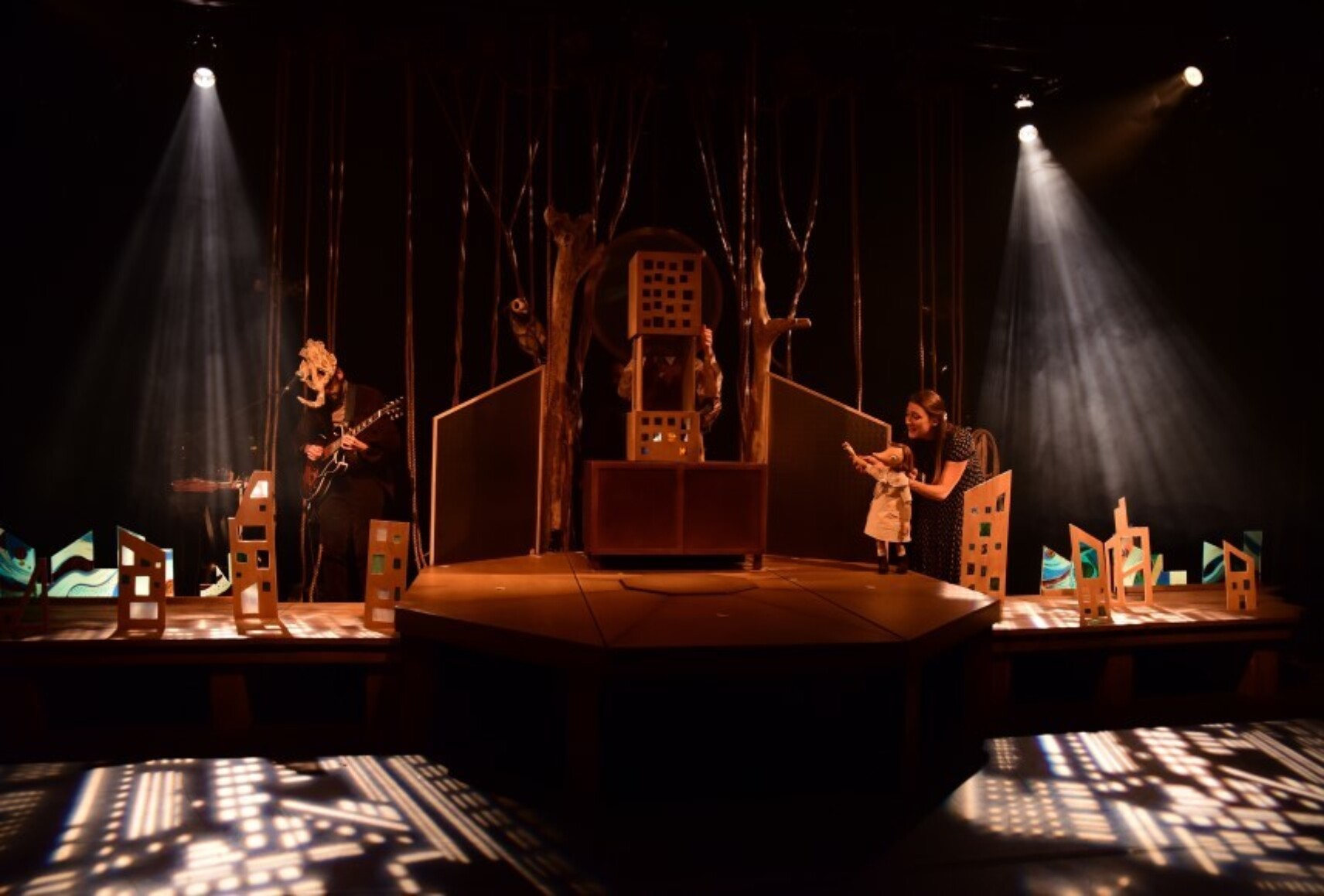 Photo de l'espace scénique avec de nombreuses structures en bois et en carton. Une comédienne manipule une marionnette.