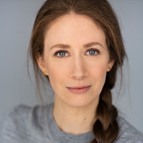 Albane a les cheveux roux tressés, la peau claire et les yeux bleus. Son visage est détendu et elle regarde la caméra. Elle porte un chandail gris et le fond de la photo est gris également.
