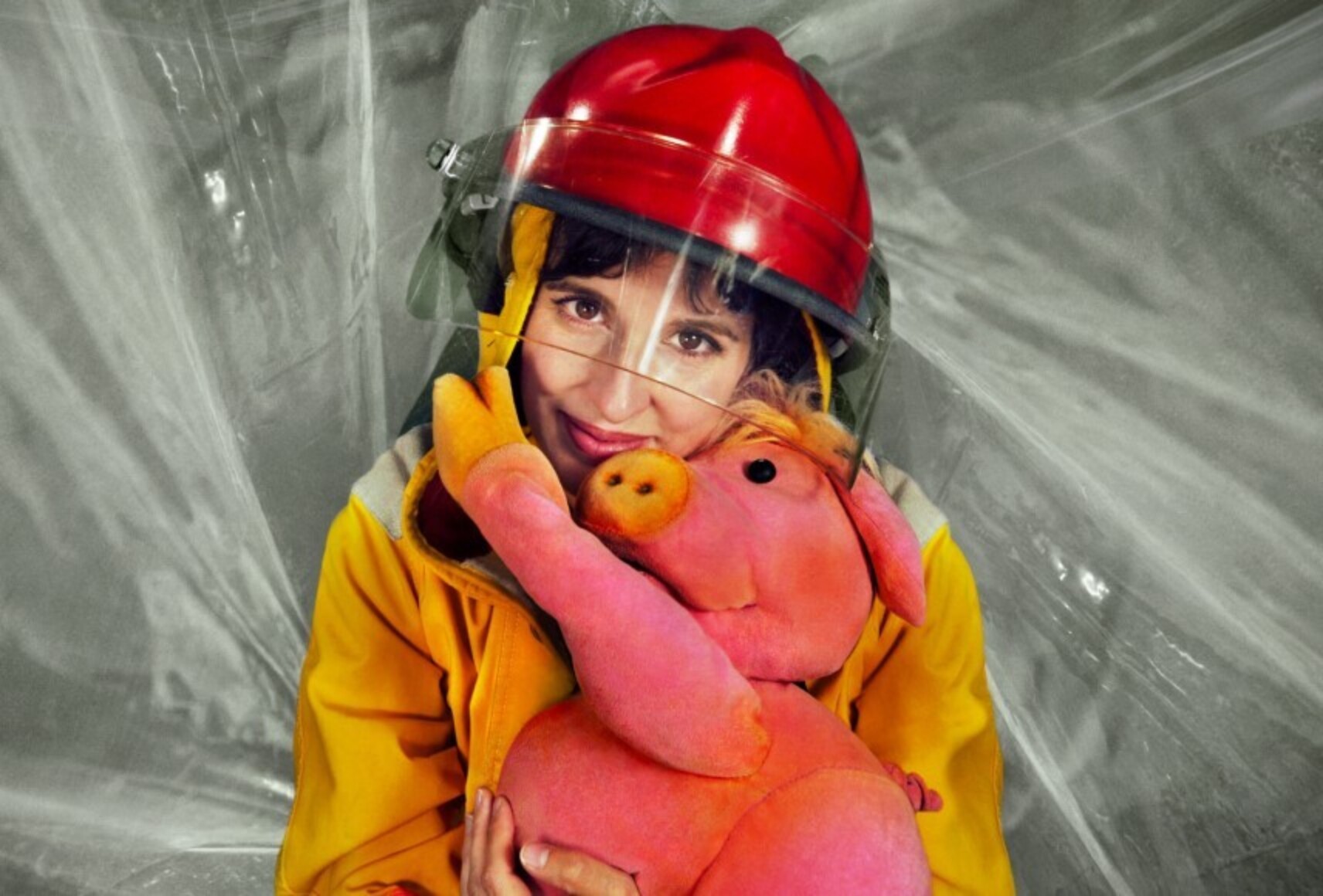 Madame Pin Pon, en combinaison de pompier, étreint le petit cochon dans ses bras. Elle sourit en regardant la caméra. Le petit cochon pose sa patte près du visage de Madame Pin Pon.