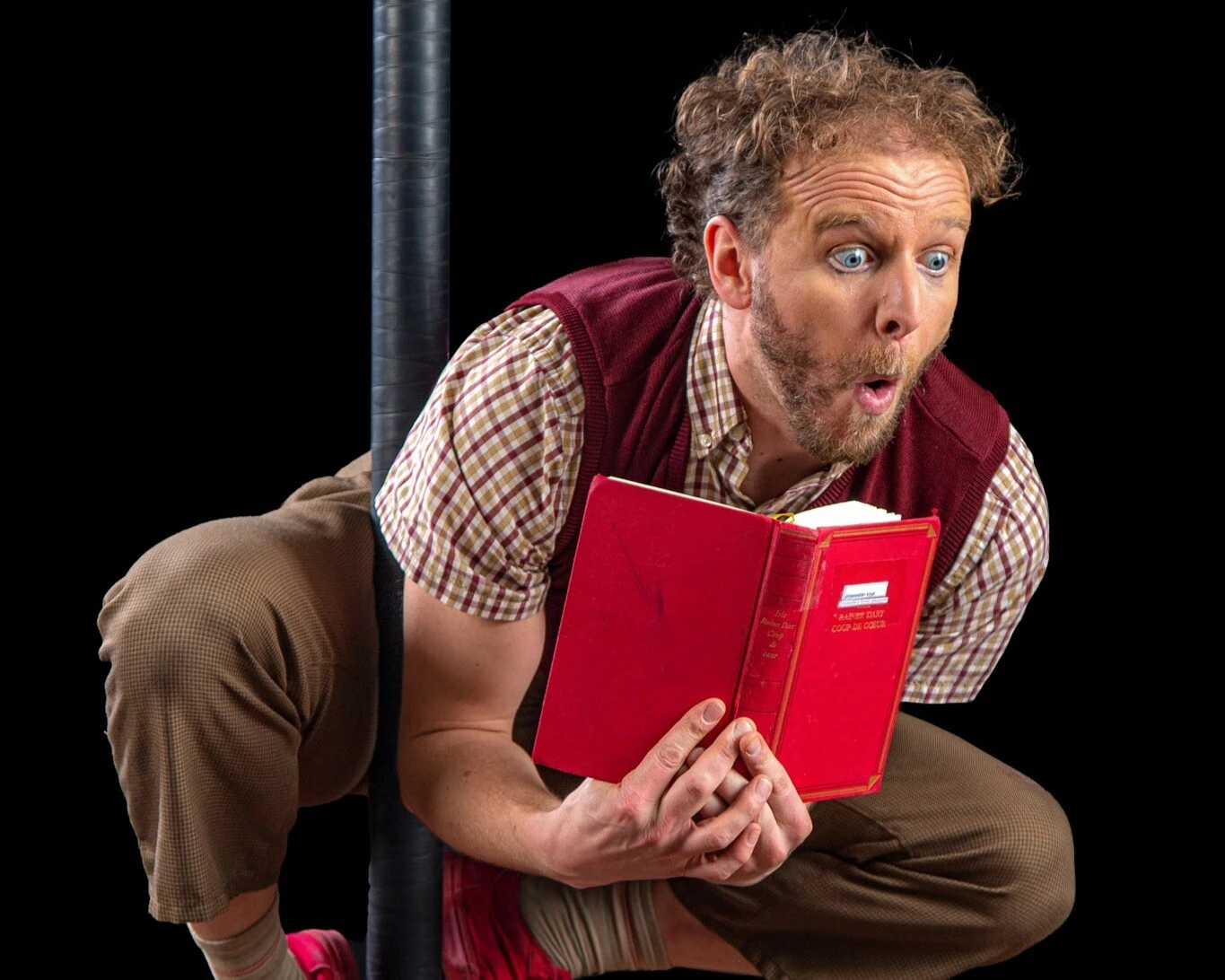 Acrobate clown accroché par les pieds à un mat entrain de lire un livre