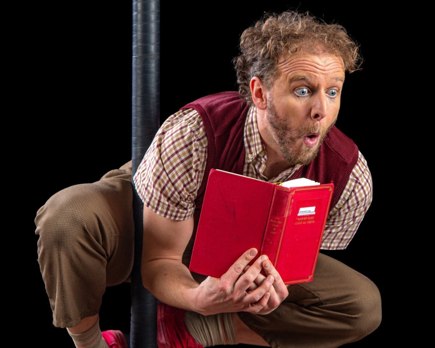 Acrobate clown accroché par les pieds à un mat entrain de lire un livre