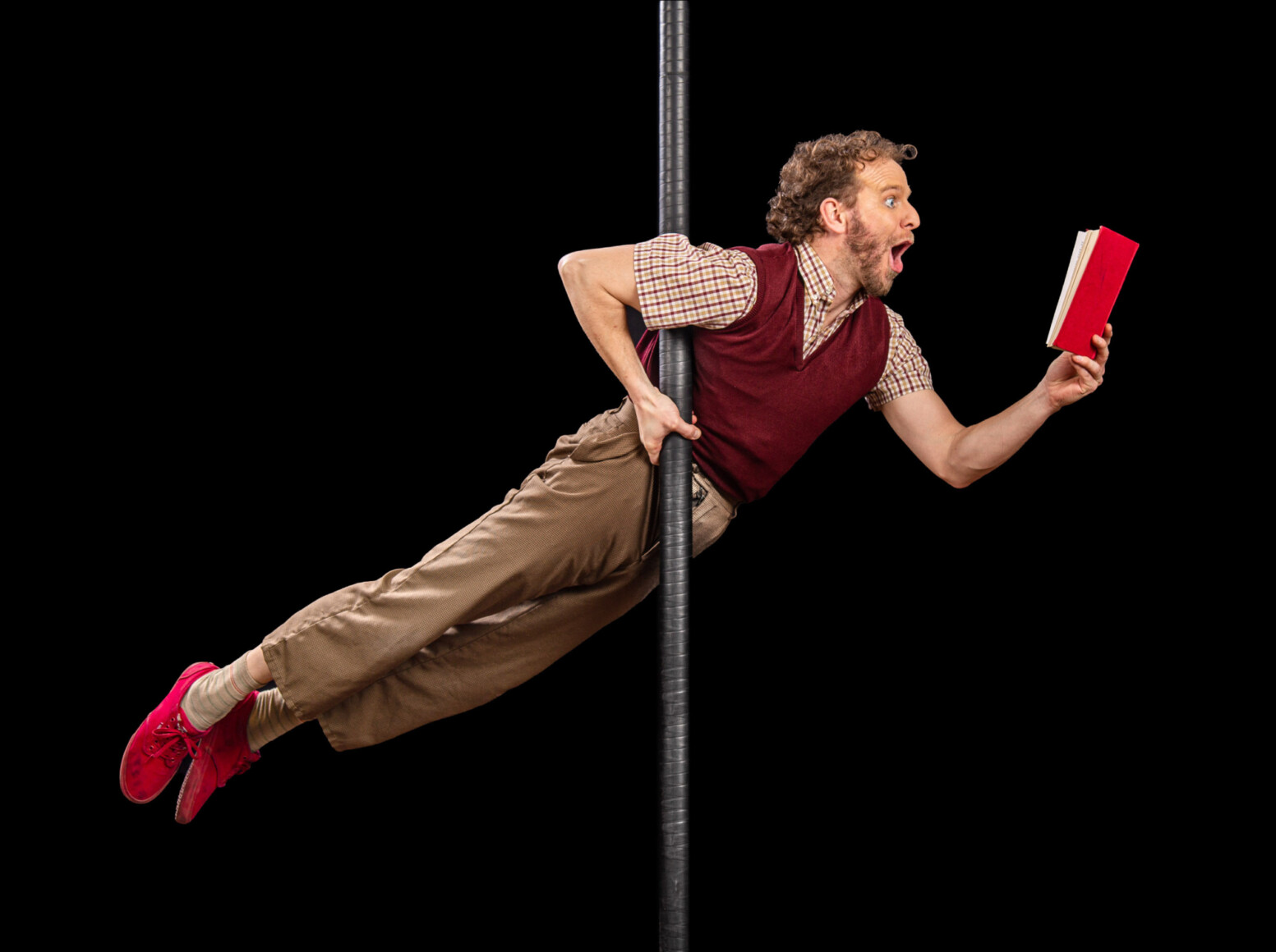 Acrobate clow accroché à une main à un mat entrain de s'émerveiller devant un livre