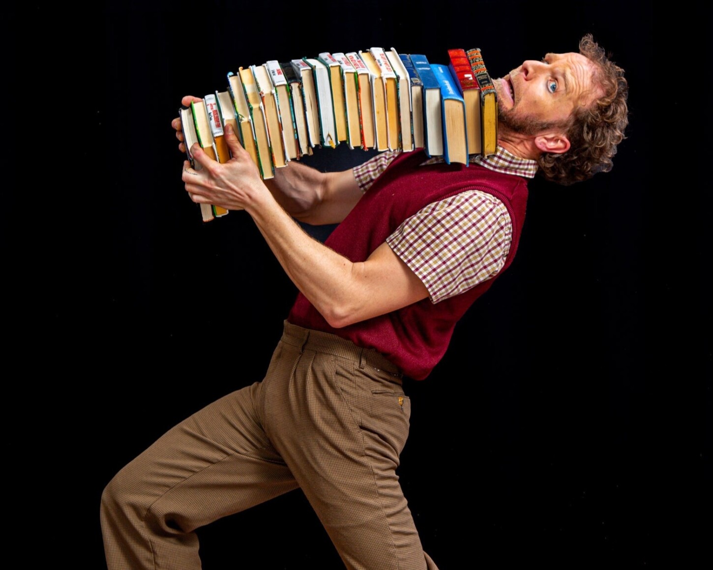 Interprête clown entrain de porter une énorme pile de livres entrain ses mains et son menton