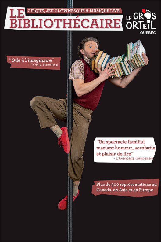 Un comédien tient en équilbre avec ses bras sur une barre verticale. Il lit un livre. Il est joyeux et étonné