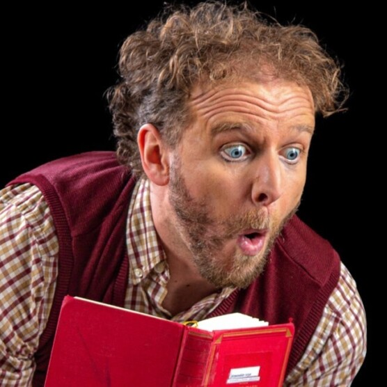 Paul-Emile Dumoulin, le bibliothécaire, lit un lire avec curiosité. Il a les yeux écarquillé et la bouche en forme de O.