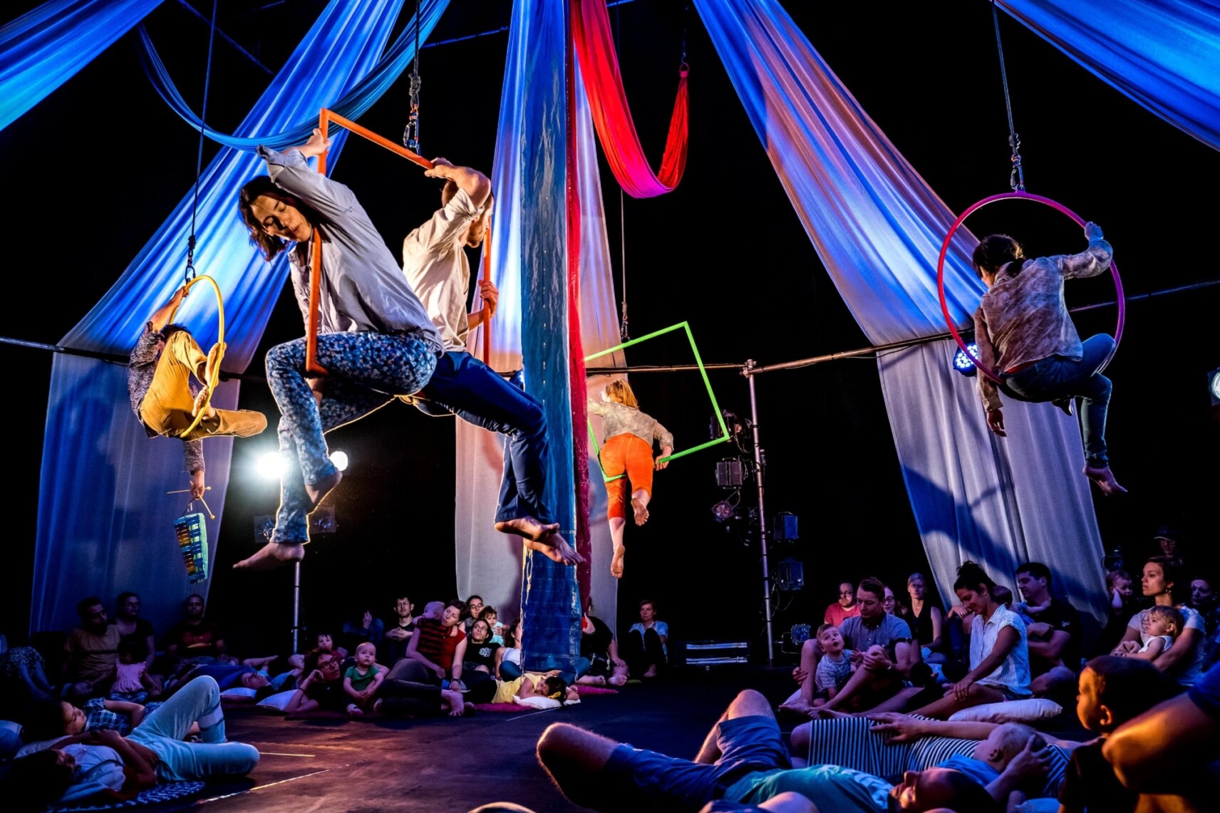 quatre artistes assis dans des cerceaux et carré aériens, chantant une berceuse au public installé sur la scène, sous eux