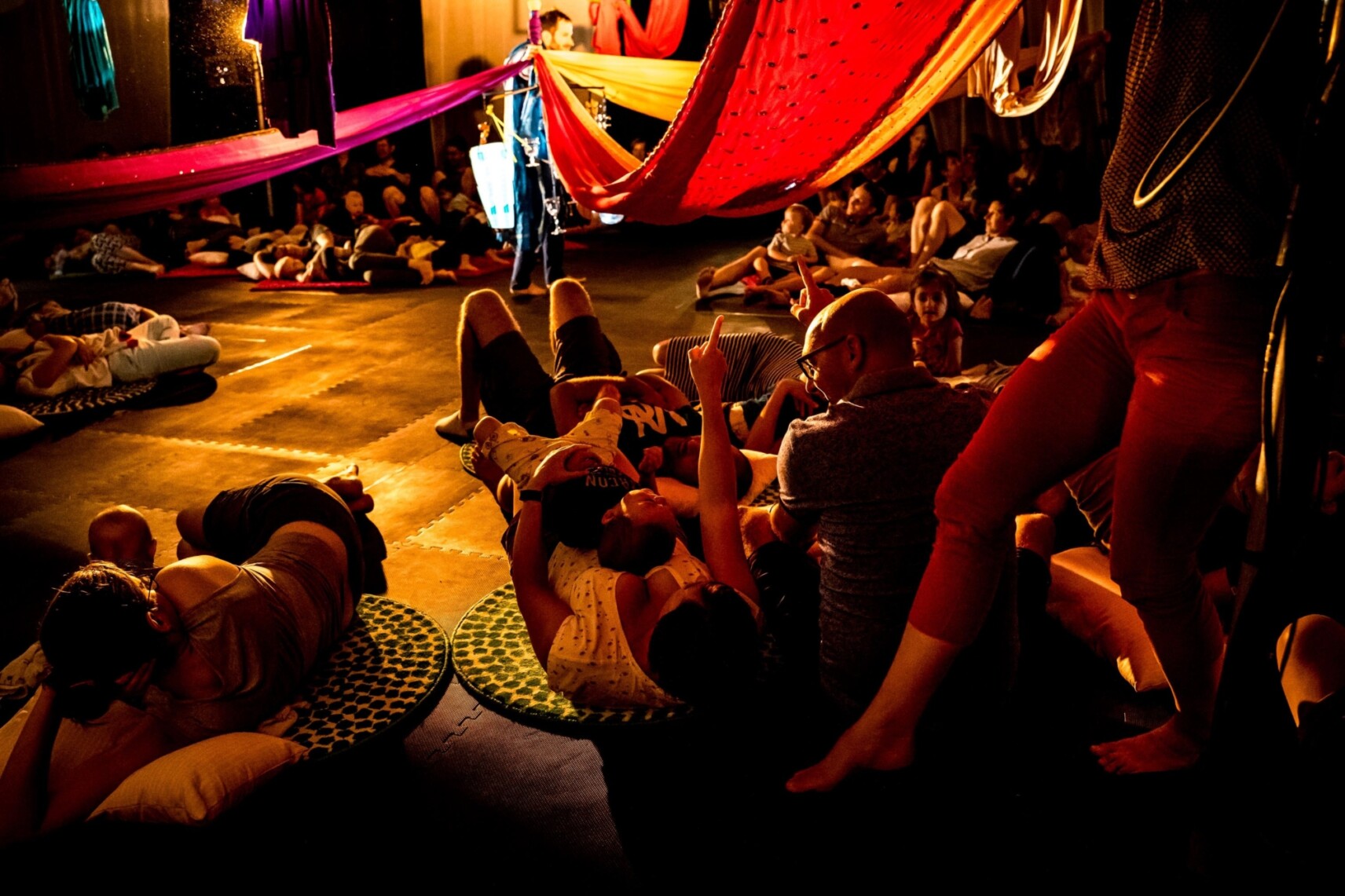 les tout-petits spectateurs et leurs parents allongés sur la scène, sous des saris colorés qui passent au-dessus d’eux