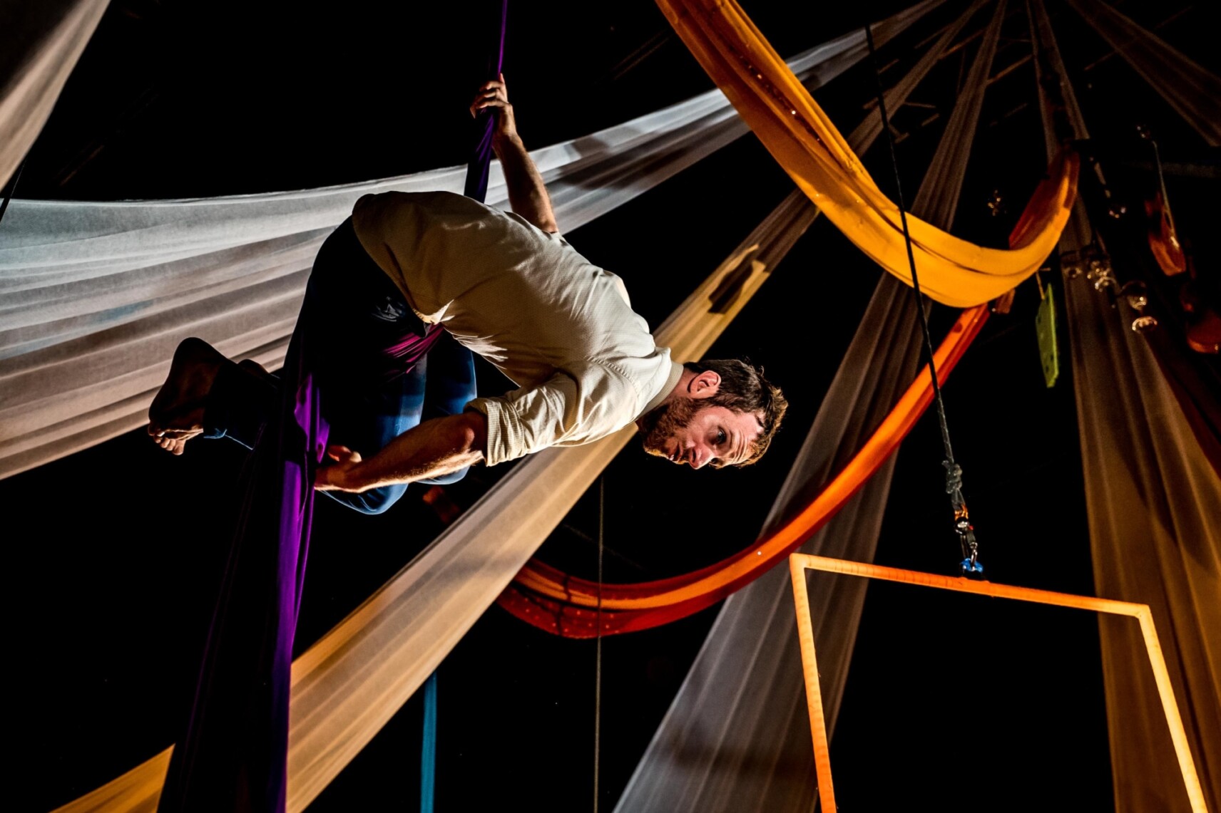 L’artiste Simon Fournier suspendu à un tissu violet, tête en-bas, regardant vers les spectateurs