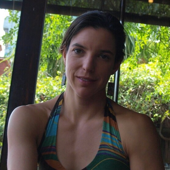 Photo portrait de l’artiste Nadine Louis, yeux et cheveux bruns, sourire timide, en robe d’été