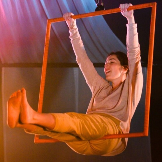 Photo portrait de l’artiste Sandy Bessette, se balançant dans un carré aérien orange