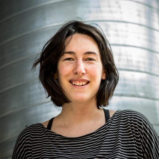 Photo portrait de l’artiste Sandy Bessette, yeux verts, cheveux bruns, sourire rieur, portant un chandail rayé noir et blanc