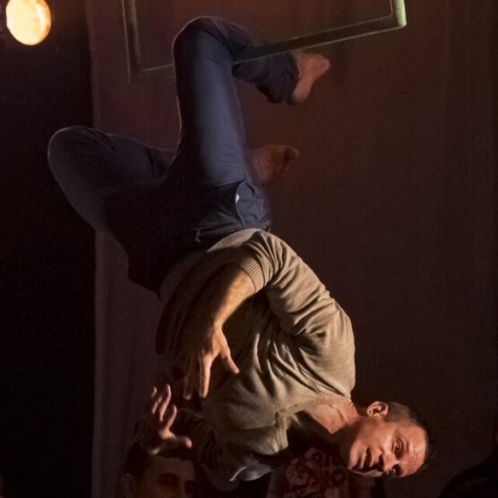 Photo en spectacle de l’artiste Simon Fournier, suspendu par un genou à un carré aérien vert