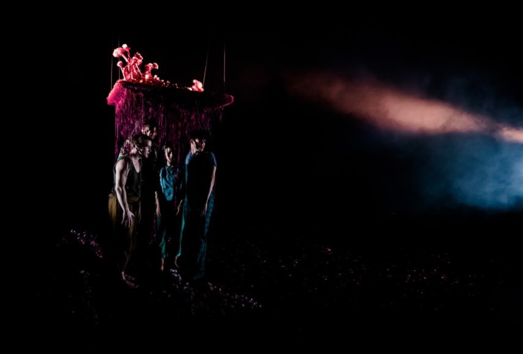Les personnages sont regroupés sous un carré de tapis rose, semblant être sous terre. Ils sont faiblement éclairés par des lumières bleu et rose.