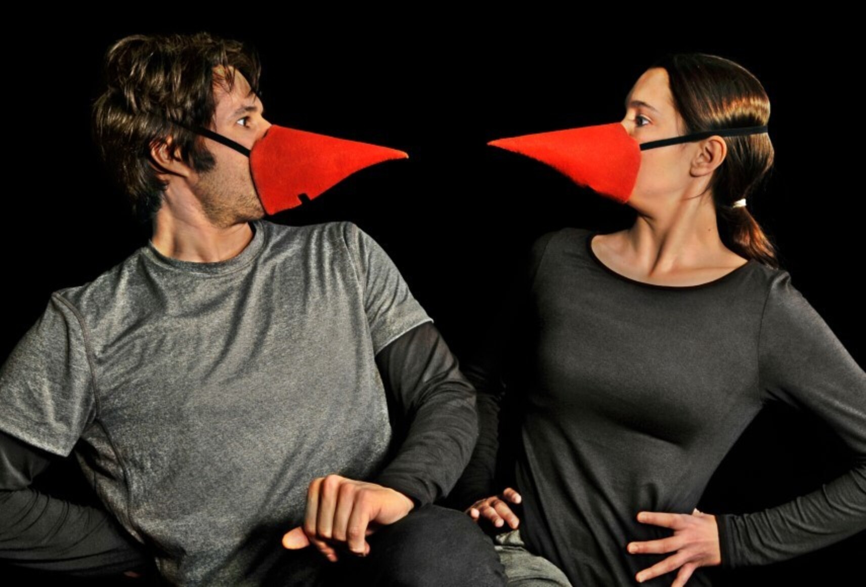 Les deux personnages sont côte à côte et se regardent, portant un masque conique rouge sur le nez.