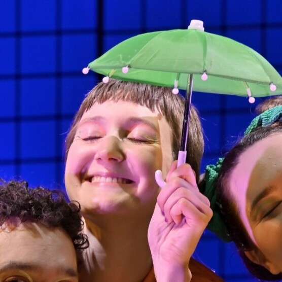 Gros plan du personnage de Coco souriant, tenant un petit parapluie vert au-dessus de sa tête.