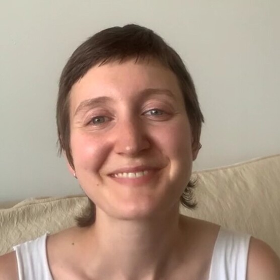 Portrait souriant d’une personne assise dans un décor neutre.