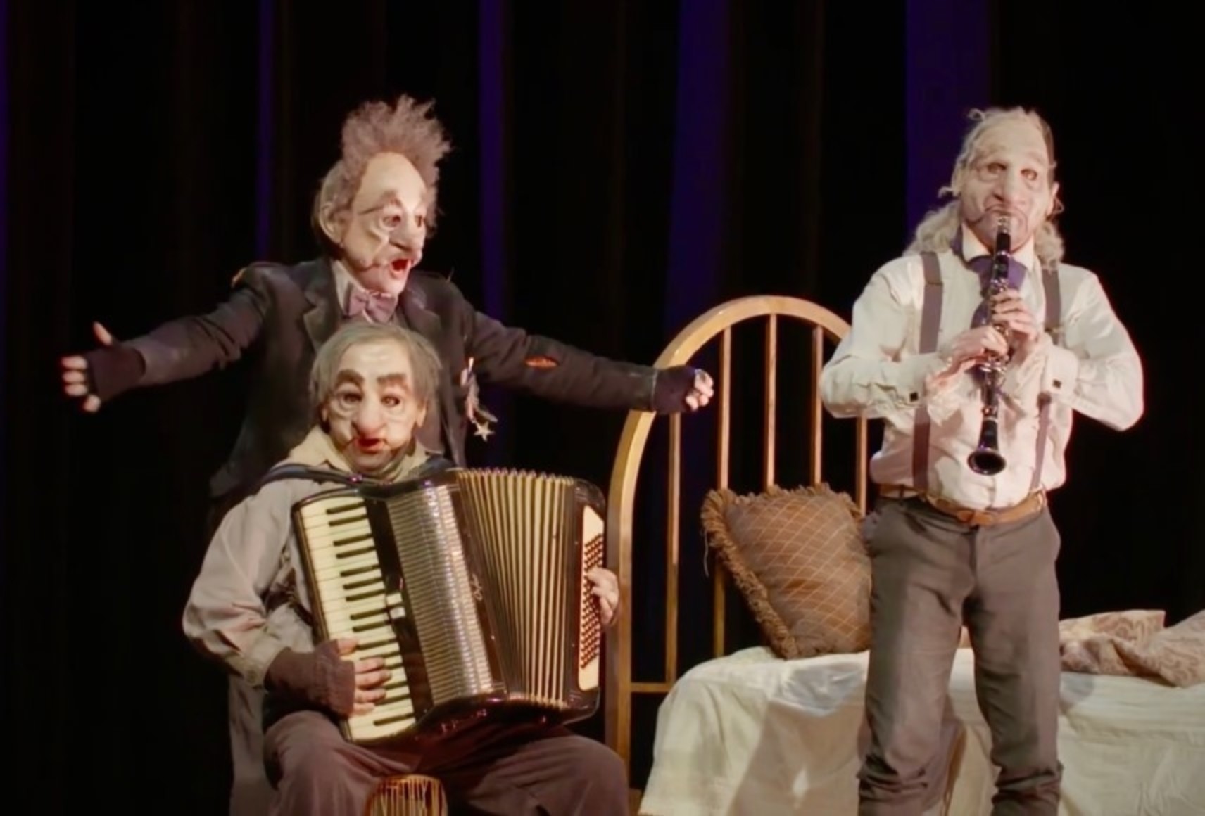 Trois personnages masqués dans une chambre. Un est assis et joue de l'accordéon, derrière lui, un autre a la bouche ouverte et les bras ouverts, comme s'il chantait. Le troisième est debout et joue de la clarinette.