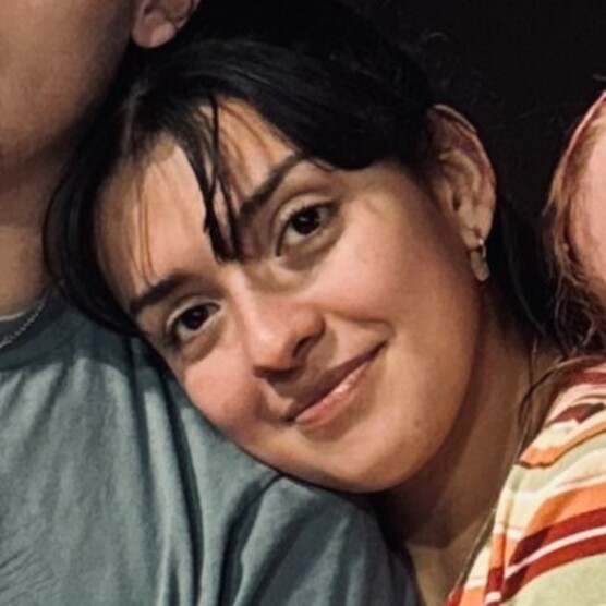 Le personnage de Désir est partiellement appuyé contre l’épaule du personnage de Mowgli et porte un vêtement à rayures orange, jaune et blanc. L’arrière‑plan est sombre, ce qui met en contraste les vêtements colorés au premier plan.