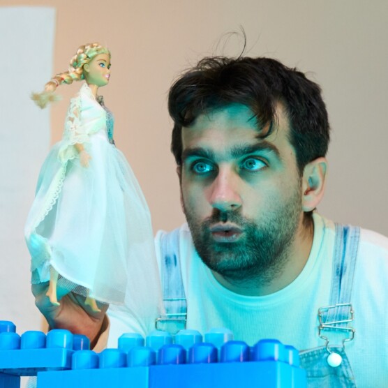 Le comédien Jonathan Hardy tient Hel, la Reine des morts, représentée par une Barbie vêtue de blanc , sur un pont de blocs bleus