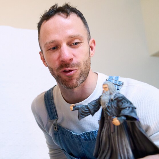 Le comédien Simon, en t-shirt blanc et salopette bleue, tient une figurine de Gandalf, qui représente Odin dans le spectacle.